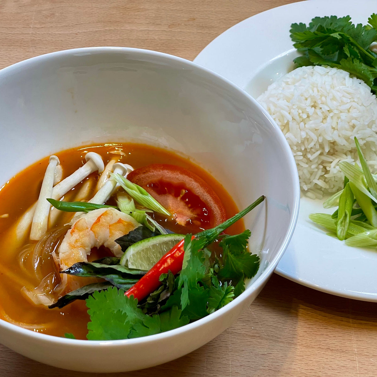 a bowl of soup next to rice and garnishes
