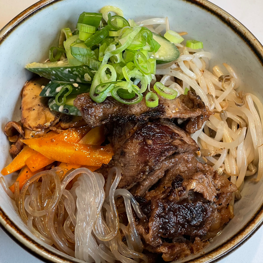 A bowl of Korean Bulgogi Beef & Glass Noodles with sliced beef, glass noodles, and vegetables garnished with green onions.