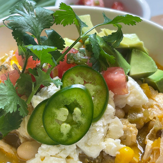 Bowl of chicken chili garnished with sliced jalapeno, avocado 
